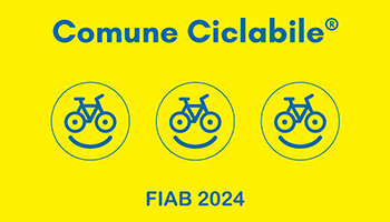 Bandiera fondo giallo e scritta blu Comune Ciclabile, scritta blu FIAB 2024, nel mezzo tre "smile" sorridenti con ruote di bici al posto degli occhi e manubrio e sella come sopracciglia